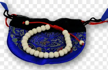 A white bead bracelet with red cord resting on a blue embroidered pouch on a transparent background.